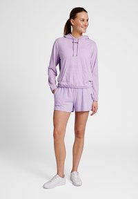Ljuslila hoodie och matchande shorts i mjukt tyg. Hoodien har en ficka fram och en dragsnodd i huvan. Vita sneakers fulländar looken.