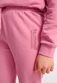 Conjunto deportivo rosa con una textura suave, que ofrece un ajuste ceñido. Logotipo grabado en el lateral del pantalón. Cintura con cordón para ajustar.