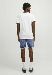 Camisa de algodón blanca, pantalones cortos de mezclilla enrollados, calcetas al tobillo y zapatos azul oscuro. Mangas cortas y diseño de cuello redondo estándar.