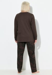 Maglietta a maniche lunghe marrone e pantaloni, con un motivo paisley nero, realizzati in un tessuto morbido. Polsini visibili e vestibilità rilassata.