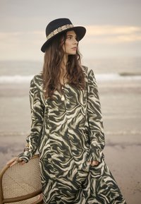 Vestido de manga larga con un patrón ondulado en verde y crema, hecho de una tela suave. Combinado con un sombrero negro que tiene una banda decorativa.