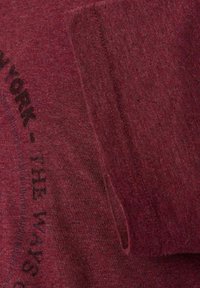 Bordowa koszulka z teksturowanej tkaniny, z czarnym nadrukowanym tekstem oraz złożonym rękawem z gładkim detalem szwu.