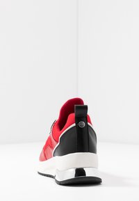 Baskets rouges et noires avec une tige en cuir lisse, un col rembourré, une semelle blanche, un accent métallique au talon et des détails en tissu texturé.
