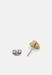 Gylne hjerteformede øredobber med metallpost og bakparti. Glatt overflate med shiny finish; bakpartiet har et design med to løkker for sikker passform.