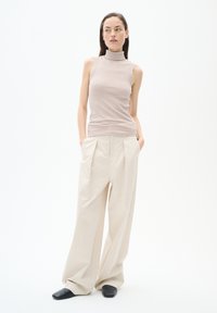 Maglione a collo alto beige a coste abbinato a pantaloni larghi oversize beige chiaro e scarpe slip-on nere. Tessuto morbido.