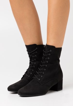Stivali alla caviglia in suede nero con tacco a blocco, caratterizzati da una chiusura con lacci sul davanti e una zip laterale per una facile vestibilità. Texture liscia e punte affusolate.