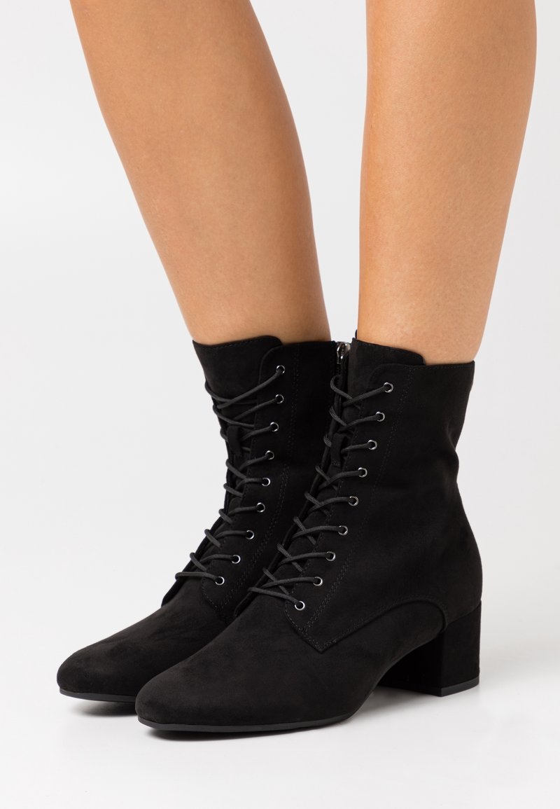 Stivali alla caviglia in suede nero con tacco a blocco, caratterizzati da una chiusura con lacci sul davanti e una zip laterale per una facile vestibilità. Texture liscia e punte affusolate.
