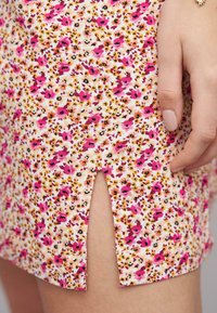 Blommig miniklänning med ett mönster i rosa, gult och svart på en ljus bakgrund; inkluderar en sidöppning och en slät tygkvalitet.