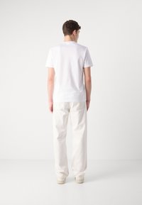 White cotton t-shirt with a round neckline, paired with loose-fitting white pants and light-colored shoes, viewed from the back.