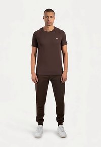 Bruine korte mouw t-shirt met een ronde hals, gecombineerd met bruine joggingbroek en witte sneakers, met een subtiel logo op de borst.