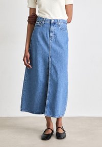 Denim maksi krilo v svetlo modri barvi s sprednjim razporkom, ki ima visok pas, zanko za pas in gumbasto zapiranje. Ujemite z črnimi balerinkami.