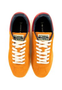 Sneakers in suede arancio con lacci bianchi, dettagli in rosso e blu navy e un'etichetta con la scritta "TENNIS" su una suola crema. Design piatto e a profilo basso.