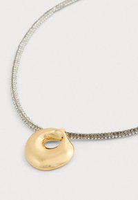 Zilveren ketting met een gladde, onregelmatig gevormde gouden hanger met een open midden, gepresenteerd op een witte achtergrond.