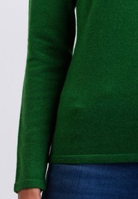 Grön ulltröja med långa ärmar, en figurnära design och en mjuk textur. Sömmen är något böjd, i kombination med blå denim.
