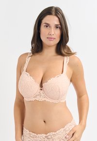 Sostenes de encaje rosa claro con patrones florales detallados, copas moldeadas y tirantes ajustables. Presenta bordes en forma de ondas y un diseño con corte central.