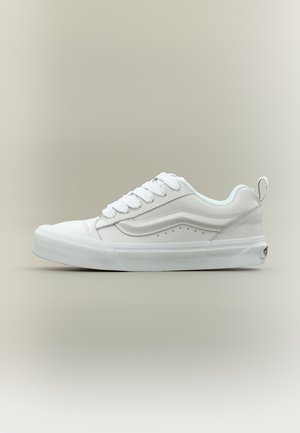 Basket blanche basse avec semelle épaisse, détail de bande latérale, col matelassé, devant lacé et languette talon sur fond neutre.