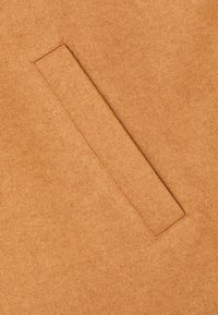 Primer plano de una tela de lana color beige con un detalle de bolsillo de welt horizontal cosido en el material.
