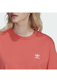 Korálově růžové tričko z bavlny, s kulatým výstřihem a krátkým rukávem, se bílým logem Adidas na hrudi.