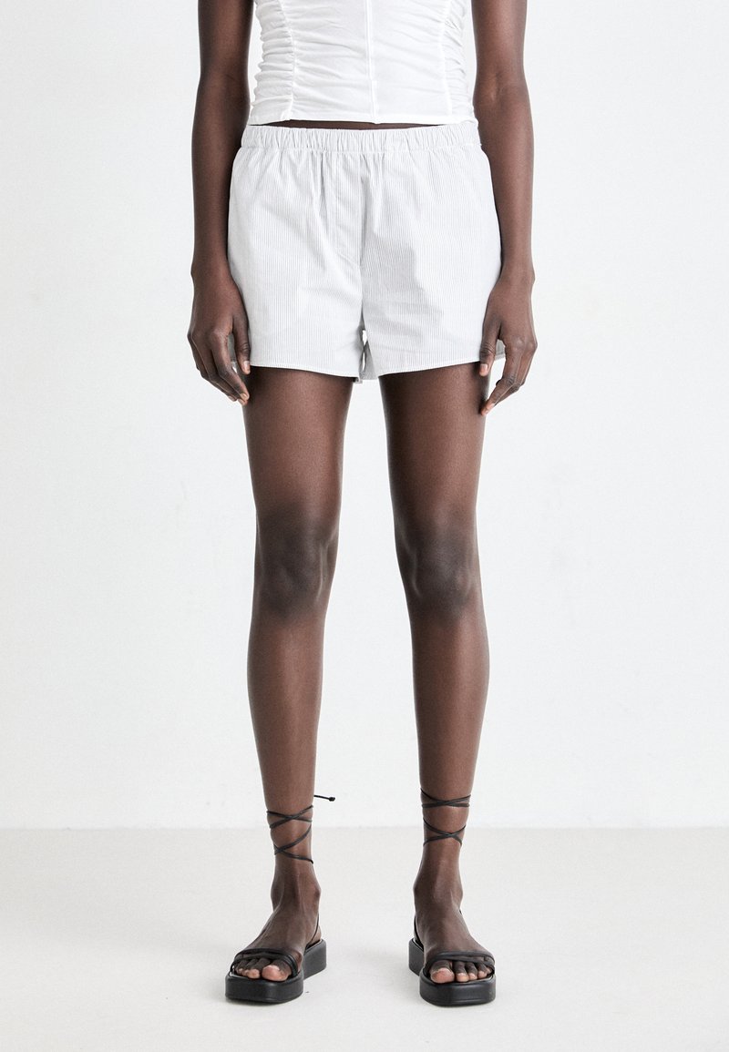 Helle grau gestreifte Shorts mit einem elastischen Bund. Kombiniert mit schwarzen, schnürlosen Sandalen. Glatte Stofftextur, lässige Passform.