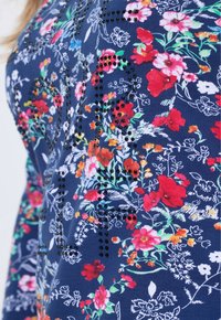 Marineblaue T-Shirt mit floralen Mustern, verziert mit mehrfarbigen Blumen und schwarzen Nieten, die dekorative Details schaffen.