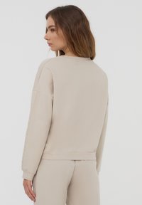 Felpa beige realizzata in materiale morbido, con una vestibilità comoda, polsini a coste e un design posteriore semplice.