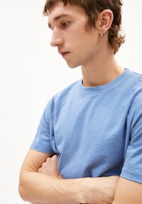 Blau gestreiftes T-Shirt aus weichem Stoff, mit Rundhalsausschnitt und kurzen Ärmeln, präsentiert an einer Person im Profil.