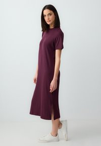 Fioletowa sukienka do kolan z krótkimi rękawami, prążkowana, z bocznymi rozcięciami, uzupełniona białymi trampkami. Prosty i minimalistyczny design.