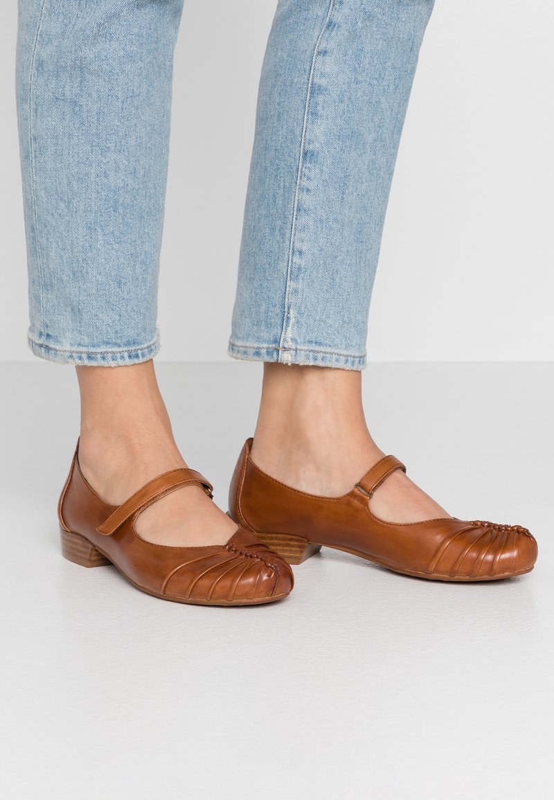Des chaussures Mary Jane en cuir marron avec un bout arrondi, des détails de plissage subtils et un petit talon bloc, portées avec un jean retroussé bleu clair.