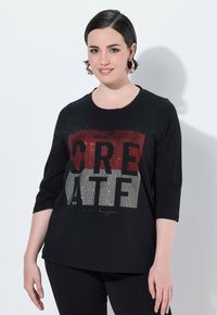 Černý top s tříčtvrtečními rukávy, který má texturovaný grafický design s nápisem "CREATE" v červené a stříbrné ozdobě.