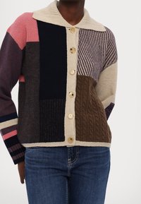 Kleurvolle, patchwork cardigan met een gebreide textuur, voorzien van een beige kraag, knoopsluiting en verschillende patronen in marineblauw, bruin en roze.