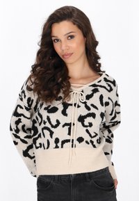 Pulover tricotat cu un model abstract bej și negru, av�ând un guler larg, detalii cu șnur și un tiv cu nervuri.