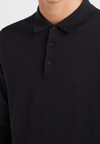 Czarna, długorękawowa koszulka polo wykonana z miękkiego materiału, z kołnierzykiem i listwą z trzema guzikami, o gładkiej fakturze, bez wzorów.