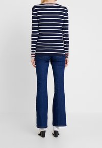 Marineblauer und weiß gestreifter Pullover mit langen Ärmeln, gerippter Struktur und kontrastierenden roten Akzenten an den Bündchen, kombiniert mit ausgestellten dunklen Jeans.