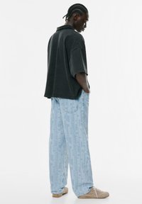 Zwarte oversized shirt met korte mouwen, gecombineerd met lichtblauwe, geblokte wijde broek. Beige sneakers maken de outfit compleet.