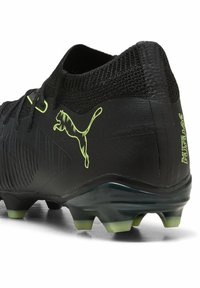 Botín de fútbol negro con superficie texturizada, acentos en verde neón, un collar tipo calcetín y una suela firme con múltiples tapones para tracción.