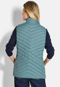 Gepolsterte Weste in hellblau mit Zickzack-Steppung, hohem Kragen und langen Ärmel in Marineblau. Lockere Passform, kombiniert mit dunklen Jeans.