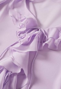 Liliowy materiał o miękkiej, lekkiej strukturze z falbaniastymi brzegami i wiązaniami. Delikatne przeszycia podkreślają warstwowy design.