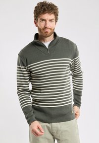 Zielono-kremowy sweter w paski z zapięciem pod szyją. Teksturowany materiał charakteryzuje się długimi rękawami i dopasowanym krojem, podkreślonym logo na dole.