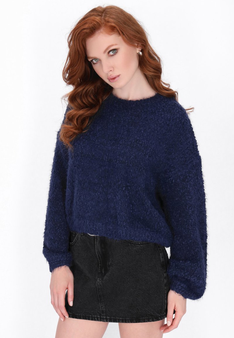 Donkerblauwe gestructureerde sweater met een ronde hals en lange mouwen, gecombineerd met een zwarte denim rok. De sweater heeft een fuzzy, zacht materiaal.