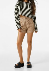 Pull court rayé noir et blanc, short beige taille haute, sandales plateformes noires, textiles lisses, ourlets de shorts retroussés.