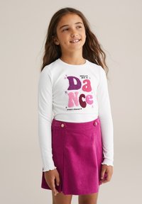 Fehér, hosszú ujjú ing, színes "DANCE" grafikával és csillagokkal, rózsaszín kordbársony szoknyával párosítva, elülső redőkkel és gombdíszítéssel.