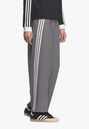 Uomo che indossa pantaloni tuta grigi a gamba larga con strisce bianche, maglia nera a maniche lunghe con maniche a righe abbinate e sneakers nere.