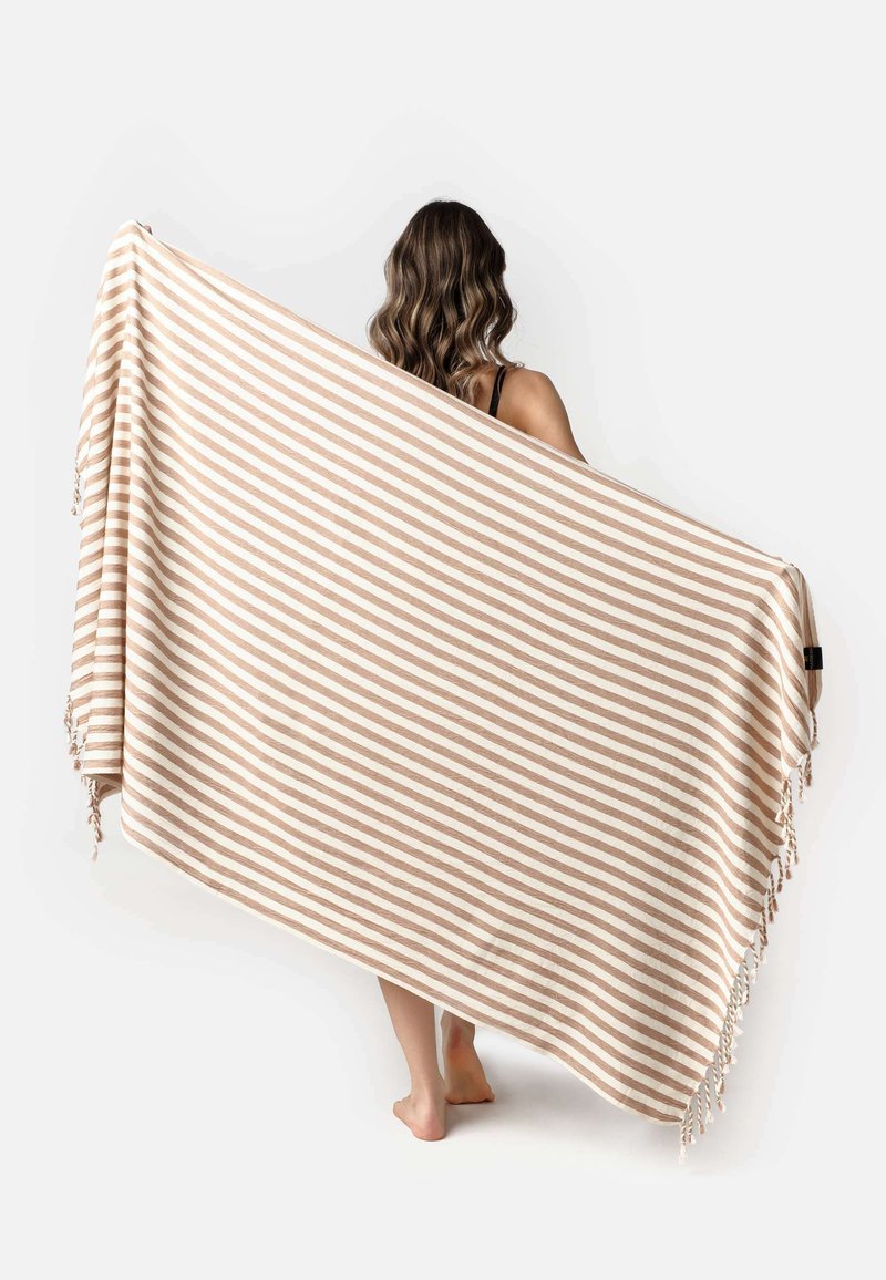 Gestreepte deken in beige en crème, met een zachte textuur, franjes langs één rand en een rechthoekige vorm.