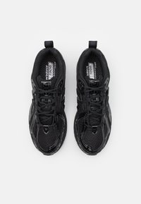 Czarne buty sportowe z siateczkową cholewką, masywną gumową podeszwą, teksturowanymi detalami oraz sznurowanym zapięciem z pętlą na pięcie.