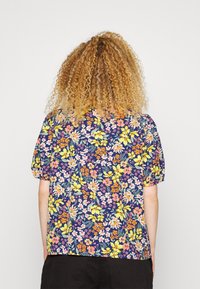 Blusa floral com mangas curtas bufantes, apresentando um fundo azul-marinho com padrões de flores rosas, amarelas e brancas. Tecido suave, corte descontraído.
