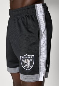 Juodos tamprės šortai su pilkomis ir baltomis šoninėmis juostelėmis, puikuojasi išsiuvinėtu Raiders logotipu. Elastingas juosmuo užtikrina tvirtą prigludimą.