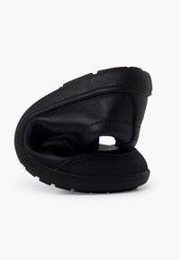 Sandale negre cu talpă joasă, prezentând un superior texturat și un branț moale. Designul este conturat, având o formă joasă și o talpă flexibilă.