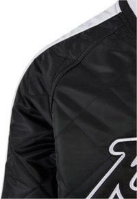 Black quilted bomber jacket featuring a glossy finish, white accent stripes, and embroidered logo detail on the front. Soft texture, structured fit.