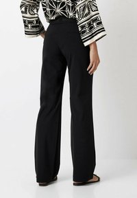 Schwarze, weit geschnittene Hose aus glattem Stoff mit einem taillierten Bund und lässiger Passform, ergänzt durch ein gemustertes, lockeres Oberteil.