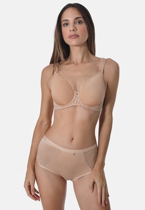 Woman modeling nude-colored bra and matching high-waist briefs with mesh detailing on a plain background.
